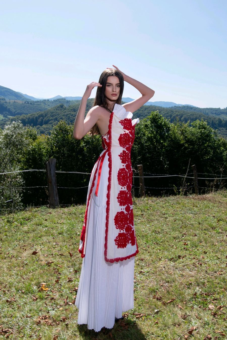 Model in red and white embroidered dress against mountains