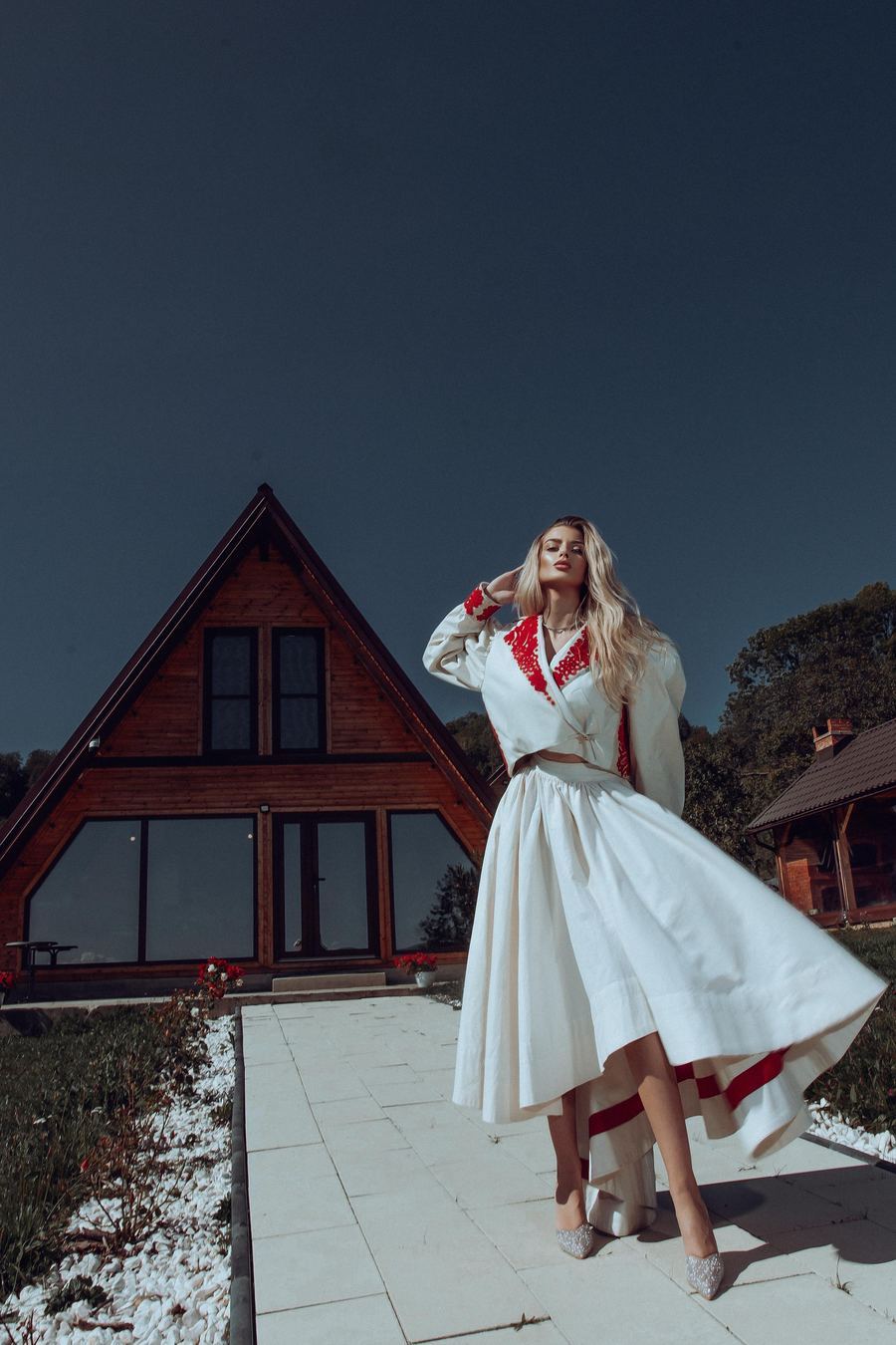 Model in white and red embroidered dress outside a Transylvanian house