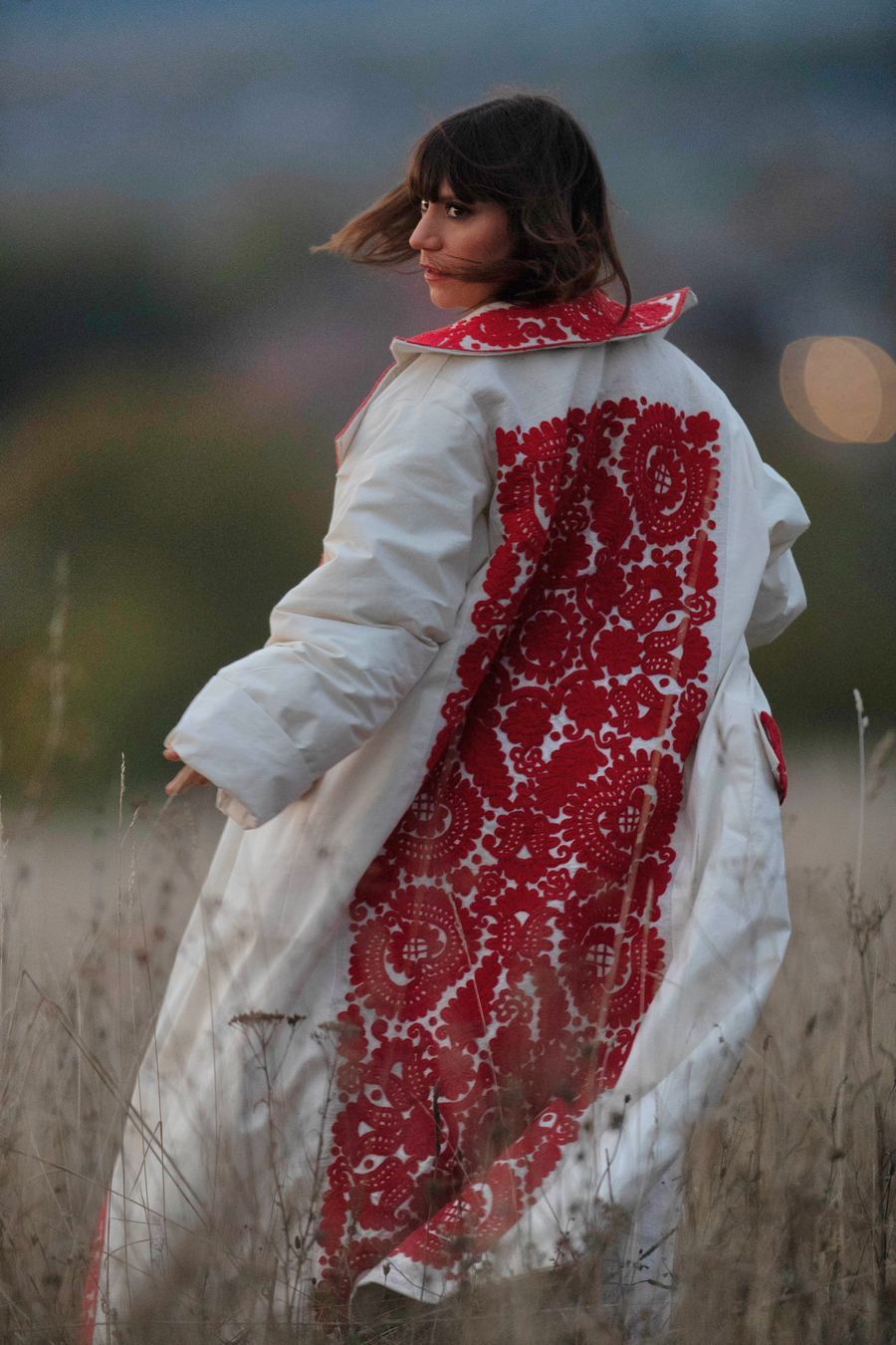 Model wearing a red embroidered coat in a dusky Transylvanian field